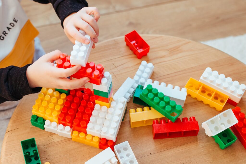a blond boy is playing with a construction kit, with a wooden wall in the background. close-up
