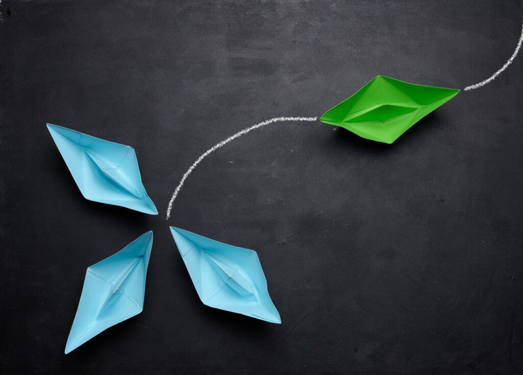 A group of blue paper boats and one is sailing away in the opposite direction