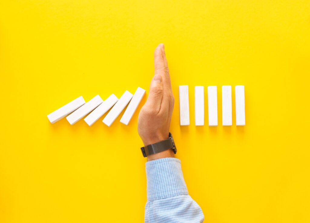 Businessman hand stopping falling dominos on yellow background. Business management crisis concept.