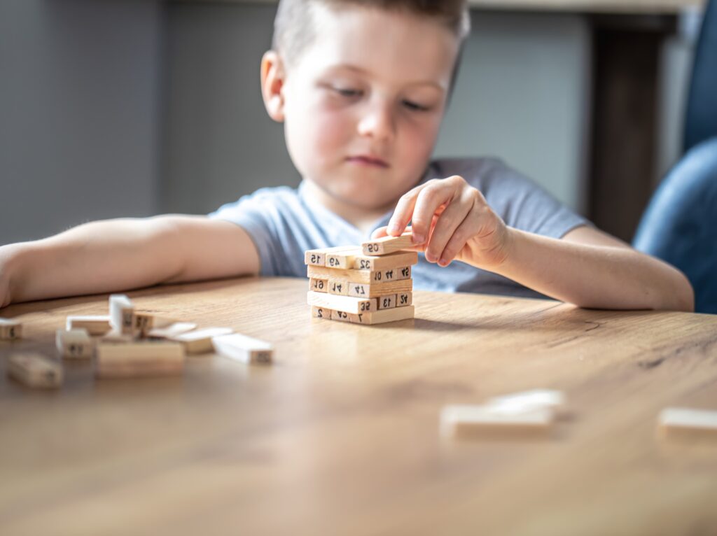 Little boy stands a turret with wooden cubes close up.