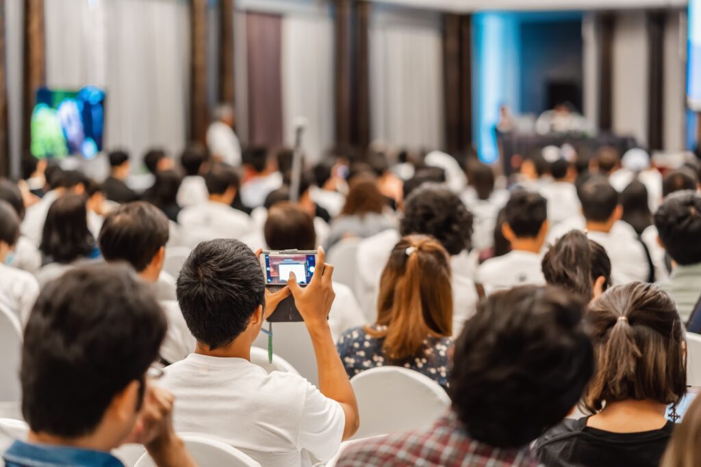 Rear view of Audience listening Speakers and using mobile phone taking the picture